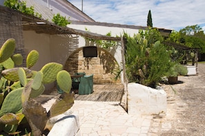 Une cour intérieure avec un mur en pierre, des plantes succulentes, une pergola en bois et un petit espace aménagé pour s’asseoir.
