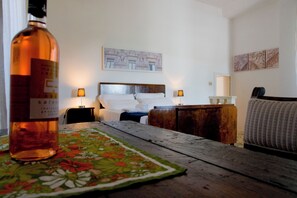Une chambre d’hôtel avec un lit, des tables de chevet, une table en bois et une bouteille d’alcool.