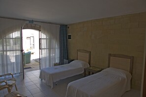 Een kamer met twee eenpersoonsbedden, een kleine tafel, een stoel en uitzicht naar buiten.