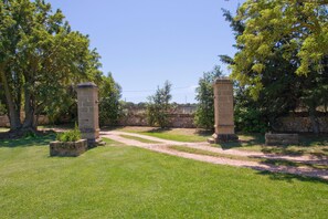 Un arco de piedra con un sendero pavimentado que atraviesa una zona cubierta de césped, con árboles y un muro de piedra al fondo.