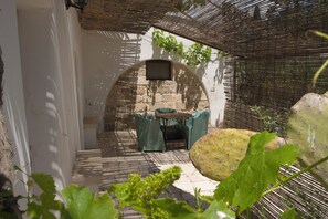 Un patio al aire libre con pared de piedra, una mesa con sillas y un televisor montado en la pared.