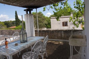 Um pátio externo com mesa, cadeiras, uma garrafa e um candeeiro.