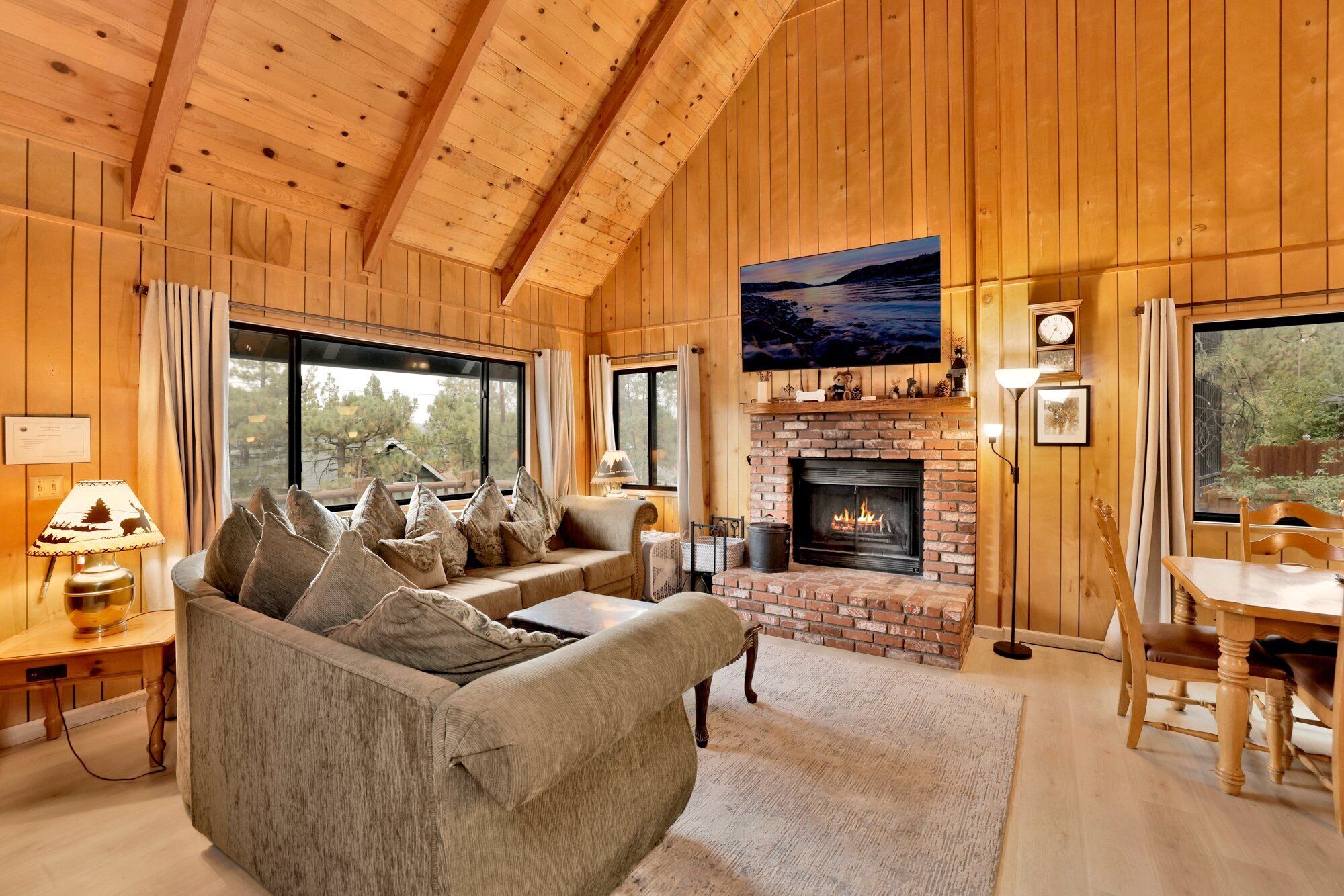 A cozy cabin interior with a fireplace, wooden walls, a sofa with cushions, and a dining area.