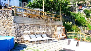 Una terraza en la azotea con un muro de piedra, una piscina inflable azul y mobiliario de exterior.