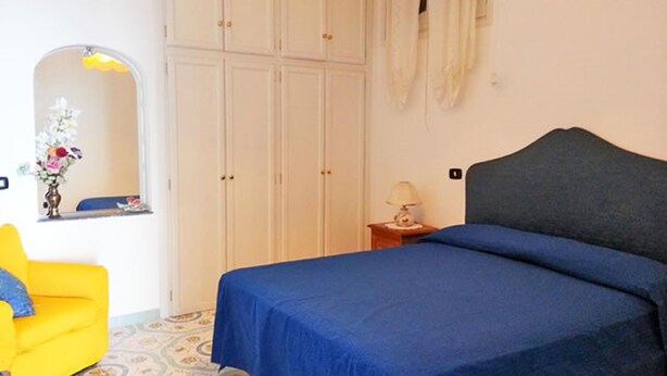 Un dormitorio con cama, mesita de noche, espejo, armario y una silla amarilla.