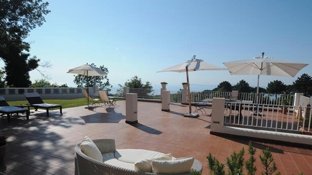 Ein Außenbereich mit Terrassenmöbeln aus Rattangeflecht, Sonnenschirmen und Meerblick.