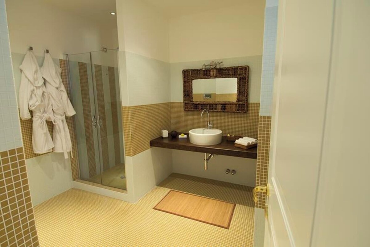 A bathroom with a glass shower enclosure, a sink with a mirror above it, and a towel rack with robes.