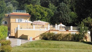 Ein zweistöckiges Gebäude mit flachem Dach, einem Balkon und einer überdachten Außenbereich-Sitzgelegenheit mit Sonnenschirmen.