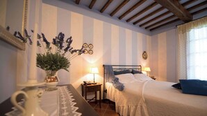A bedroom with a bed, bedside tables, a lamp, a mirror, and a vase with flowers. - Casa Lari (San Gimignano)