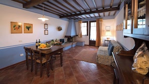A dining area with a wooden table, chairs, and a fruit bowl. There is a sofa and a piano in the background. - Casa Lari (San Gimignano)