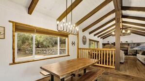Une table à manger en bois avec des bancs, un mur en pierre et une grande fenêtre donnant sur un jardin.