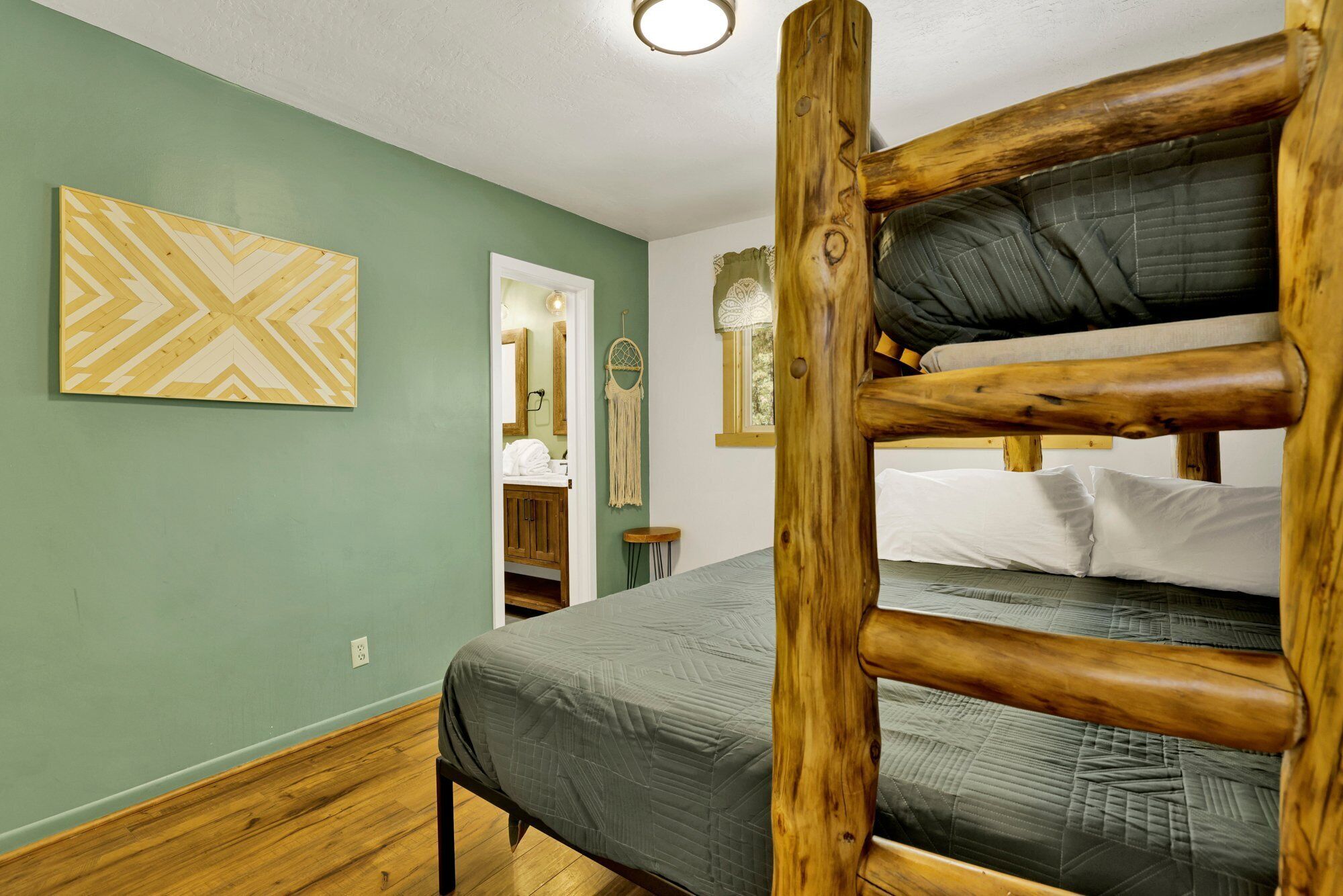 A bunk bed with a wooden frame, a green wall with a geometric patterned artwork, a mirror, and a small bedside table.