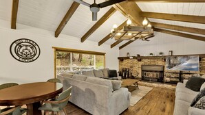 L’intérieur chaleureux d’un chalet avec une cheminée en pierre, des poutres en bois et une grande fenêtre donnant sur une forêt.