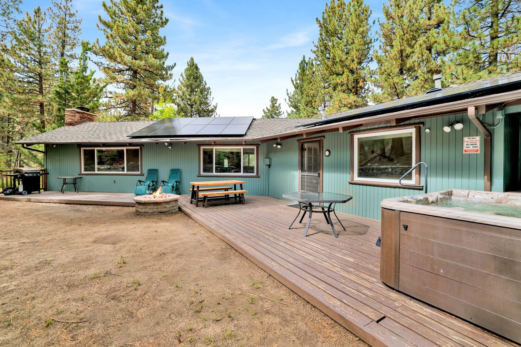 A cabin with a deck, outdoor seating, a hot tub, and a fire pit.