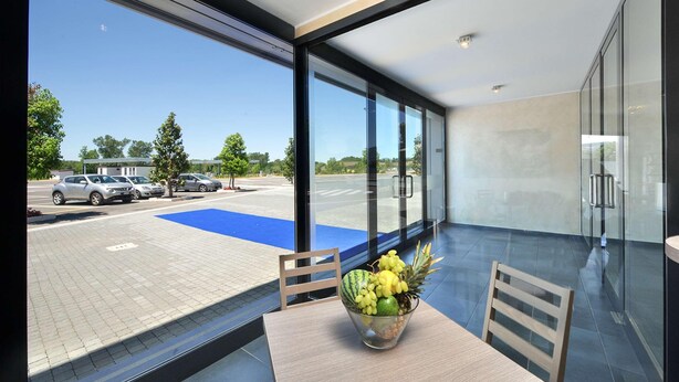 A modern hotel room with large windows, a view of a parking lot, and a table with a fruit bowl. - Testani Colleferro (Colleferro)
