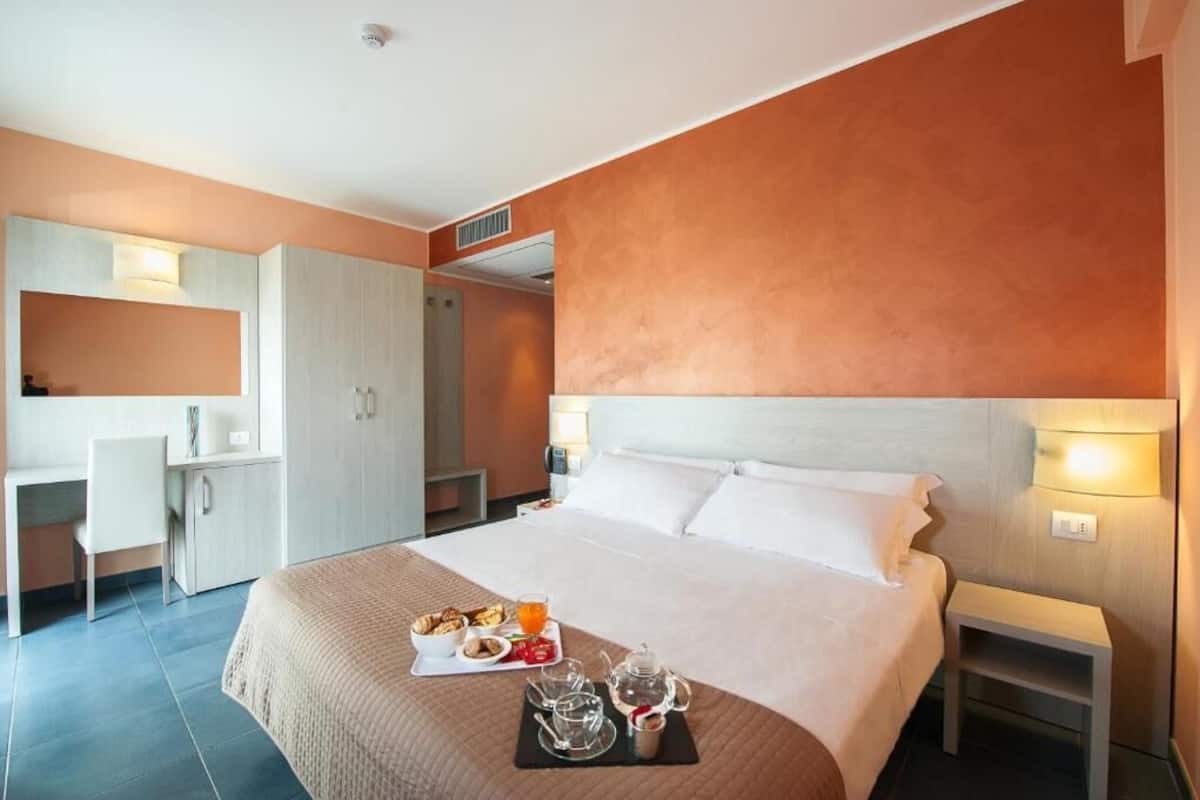 Quarto de hotel com uma cama grande, uma escrivaninha e um guarda-roupa. Há uma bandeja de café da manhã na cama.