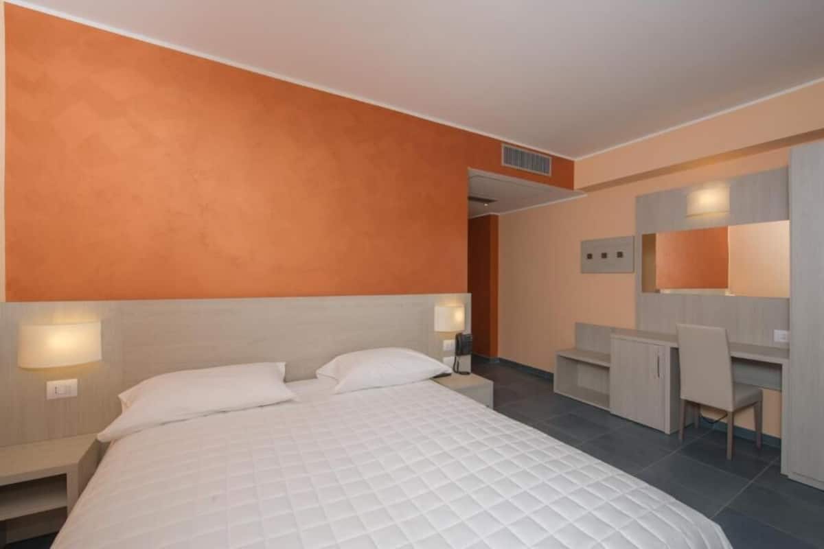 Quarto de hotel moderno com uma cama grande, uma escrivaninha e um espelho.