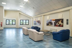 Un'ampia hall con soffitto alto, grandi finestre e un estintore appeso al muro.