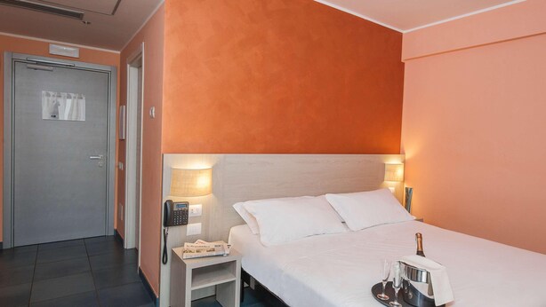 A hotel room with a bed, bedside table, and a tray with a bottle and glasses. - Testani Colleferro (Colleferro)