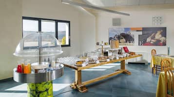 Montaje de bufé con diversos alimentos y bebidas, un ventanal con vistas y una pared con carteles informativos.