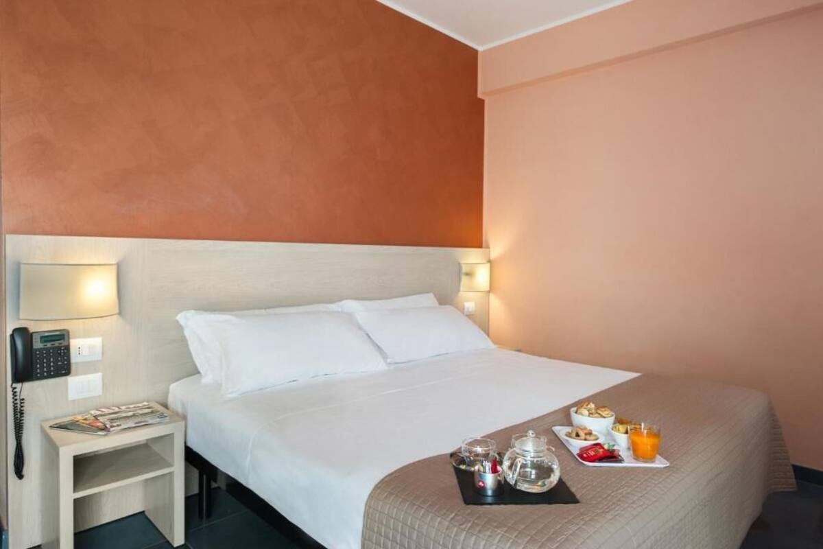 Quarto de hotel com cama, mesa de cabeceira, luminária e bandeja de café da manhã.