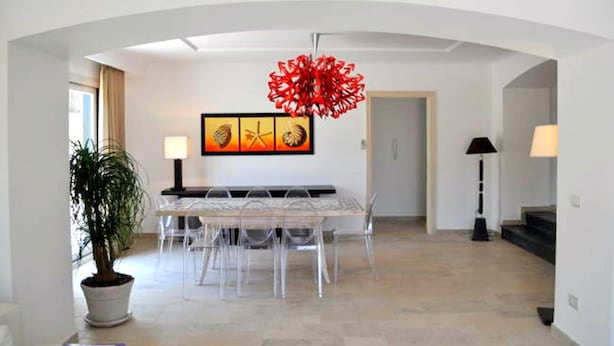 Un espace repas moderne avec une table et des chaises aux lignes épurées, une plante en pot et un lustre rouge.