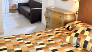 Une chambre avec une couvre-lit à carreaux, une commode, un miroir et un canapé dans la pièce adjacente.