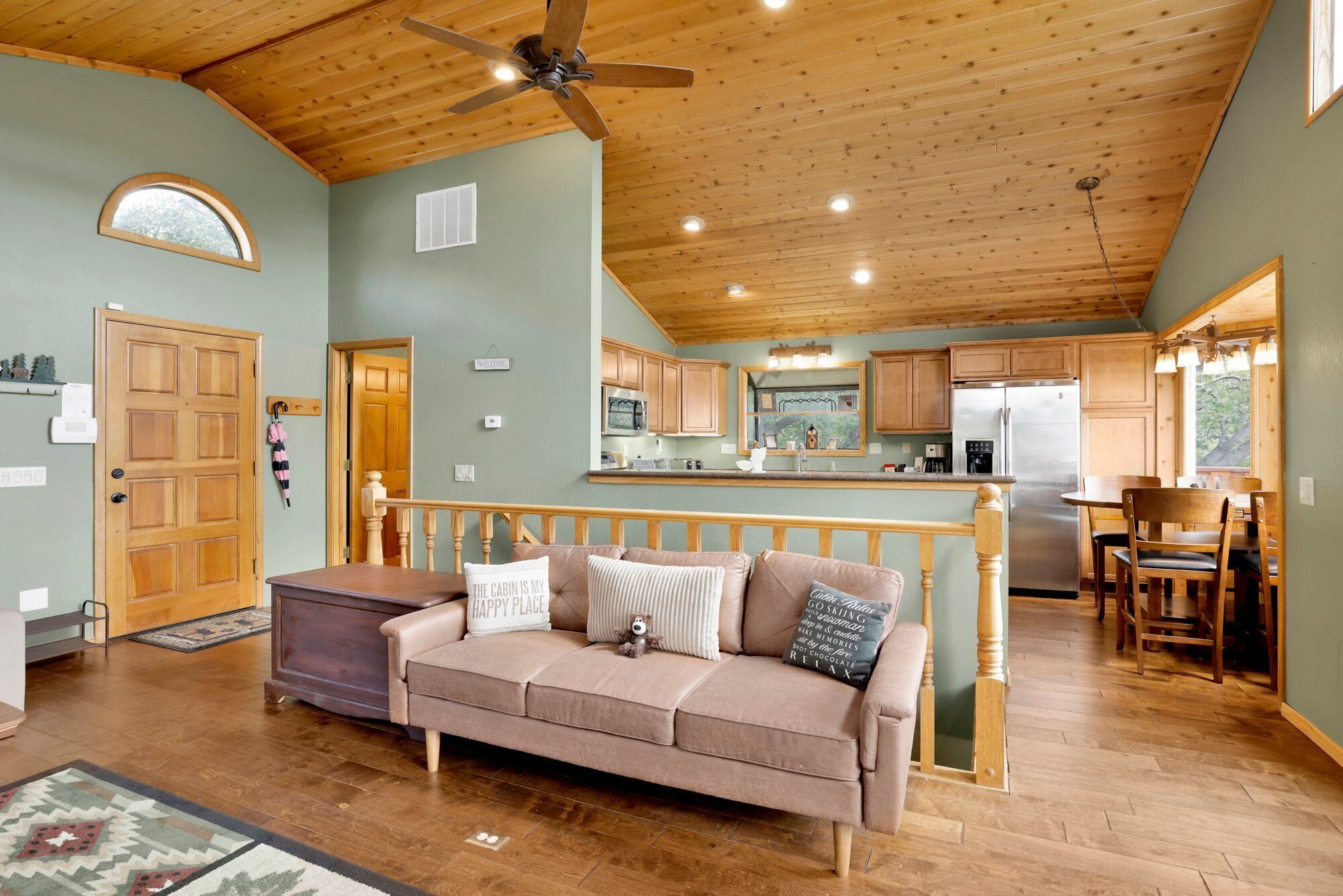 A cozy cabin interior with a wooden ceiling, a kitchenette, a dining area, and a living room with a sofa and a rug.