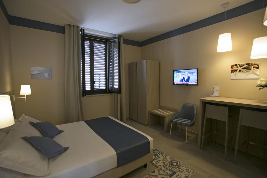 A hotel room with a bed, a desk, a chair, a television, and a wardrobe.