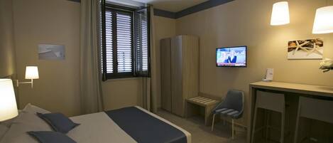 Una habitación de hotel con cama, escritorio, silla, televisor y armario.