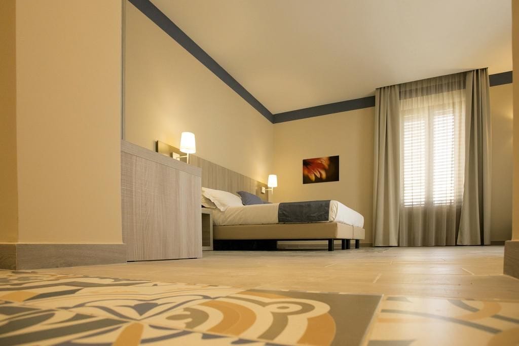 A hotel room with a bed, bedside lamps, a painting, and a large window with curtains.