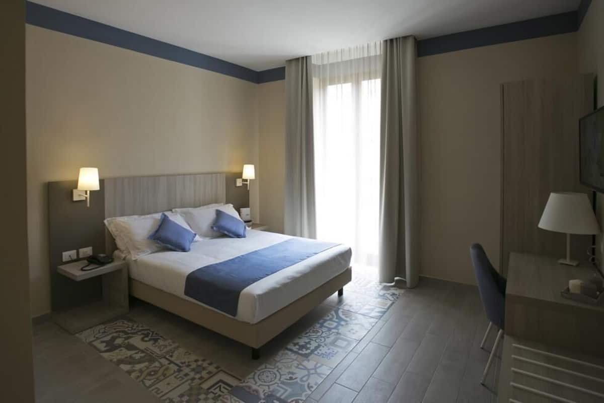 Habitación de hotel con una cama grande, dos lámparas de noche, un escritorio con una silla y un televisor en la pared.