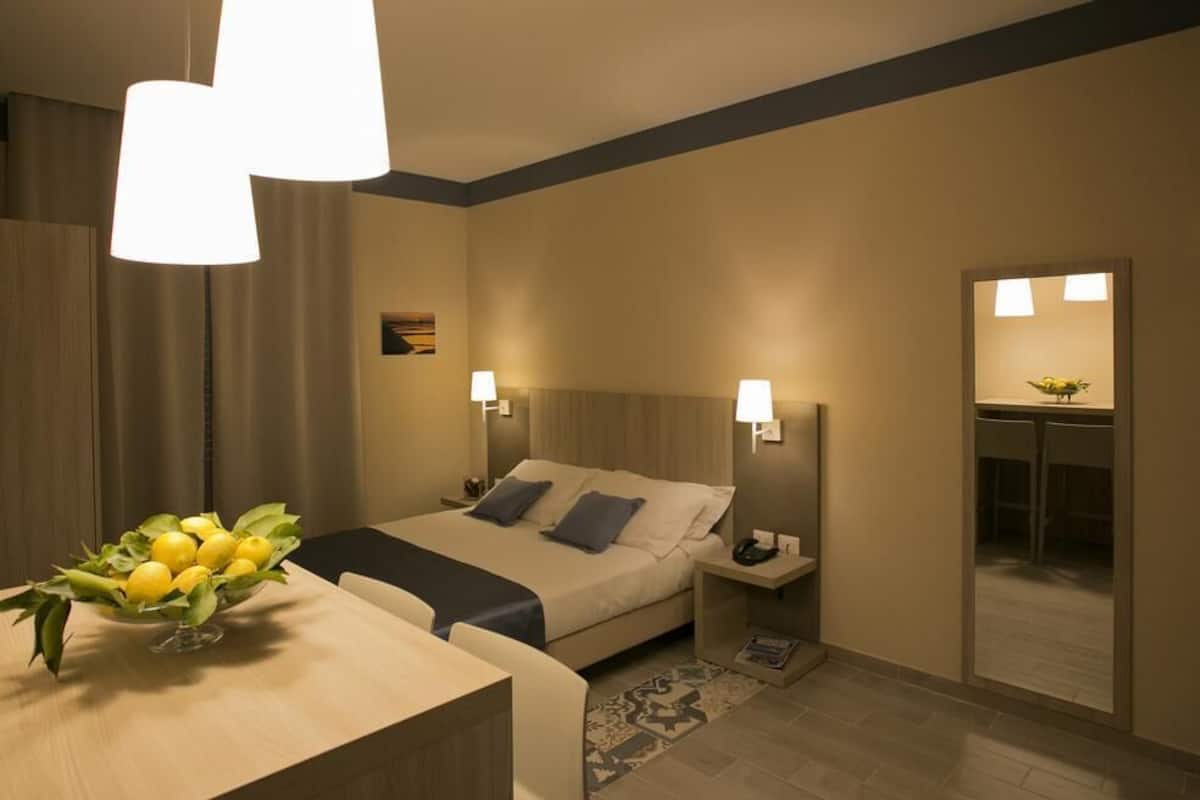 Una habitación de hotel moderna con una cama, mesitas de noche, un escritorio y un espejo.