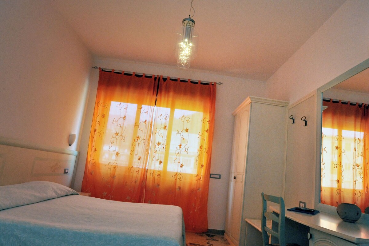 A hotel room with a bed, a desk with a chair, a mirror, and curtains.