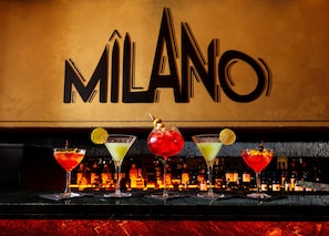 Un bar avec une enseigne « MILANO », une variété de cocktails et un assortiment de bouteilles d’alcool.