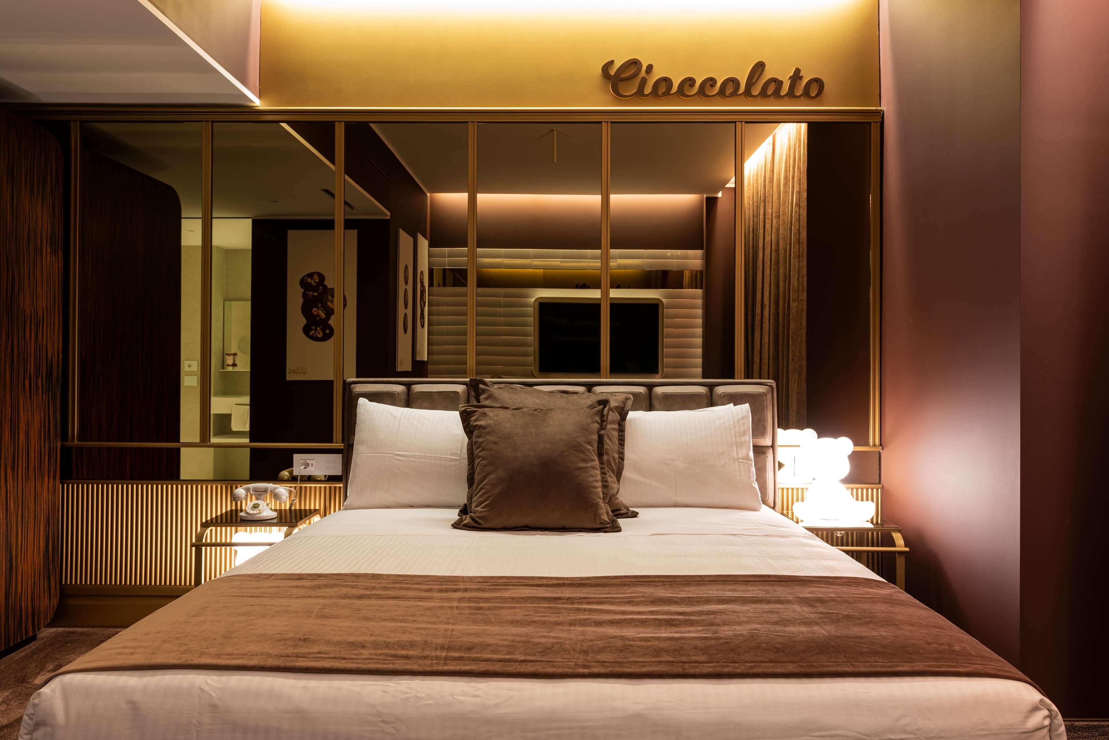 A hotel room with a bed, a nightstand, a lamp, and a mirror.