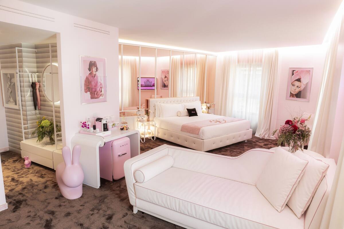 Une chambre à coucher avec un lit, un canapé blanc, une coiffeuse avec un miroir et une chaise rose.