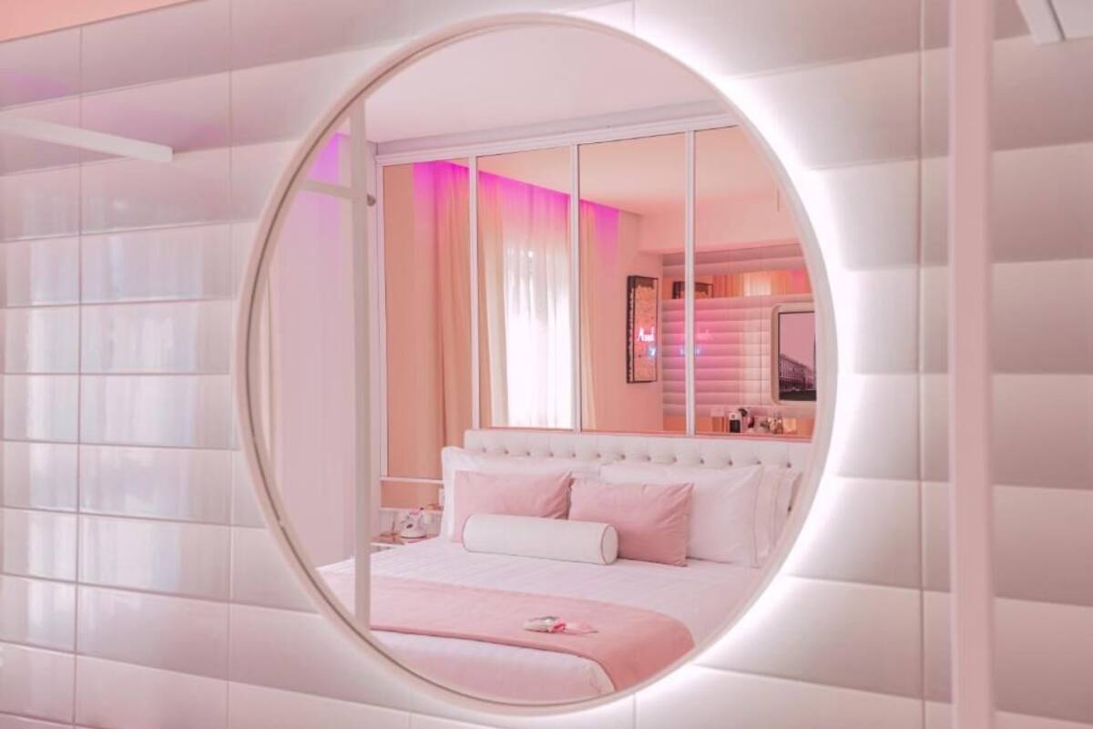 Une chambre avec un grand miroir, un lit avec une literie blanche et un mur d’accent rose.