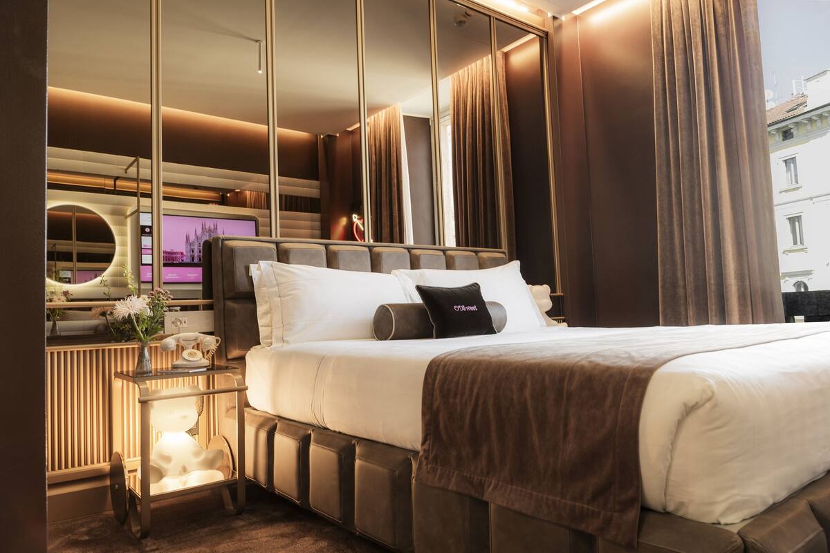 Une chambre d’hôtel moderne avec un grand lit, une table de chevet avec une lampe et un grand miroir.