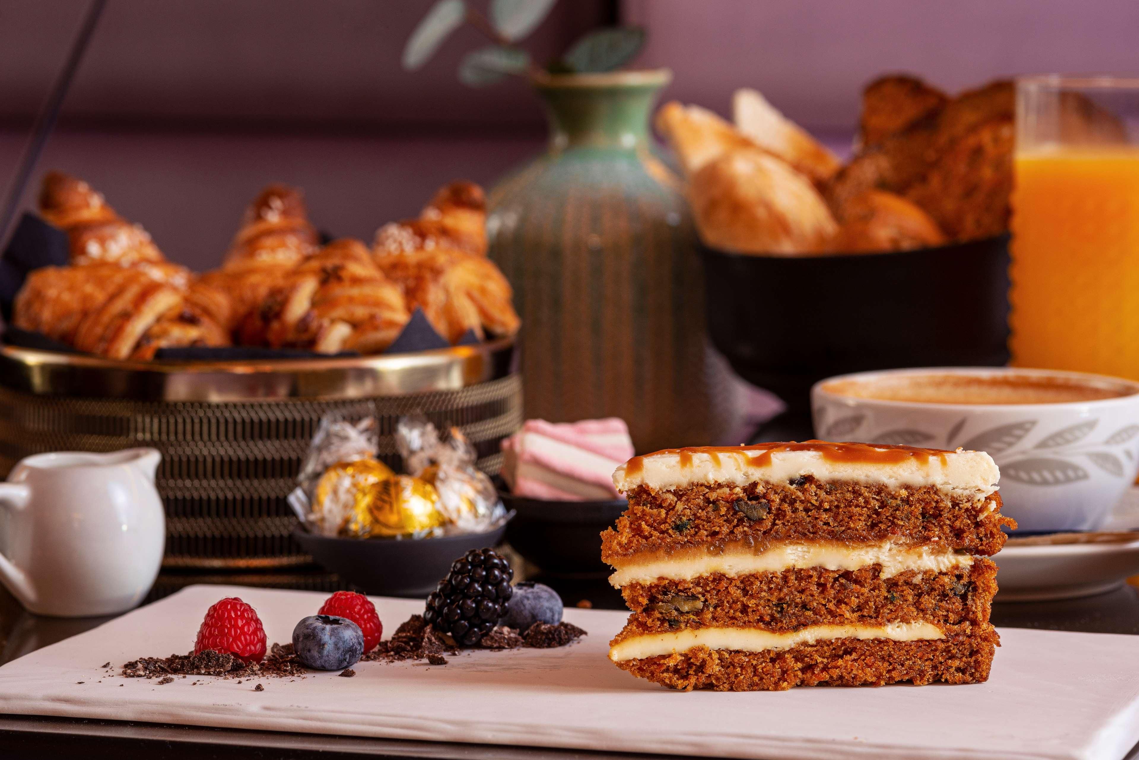 Une assiette à dessert avec un gâteau à plusieurs couches, un bol de croissants et un verre de jus d’orange.