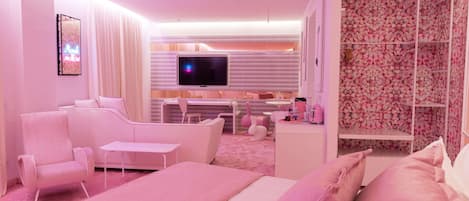 A pink-themed hotel room with a bed, a TV, a seating area, and a wardrobe.