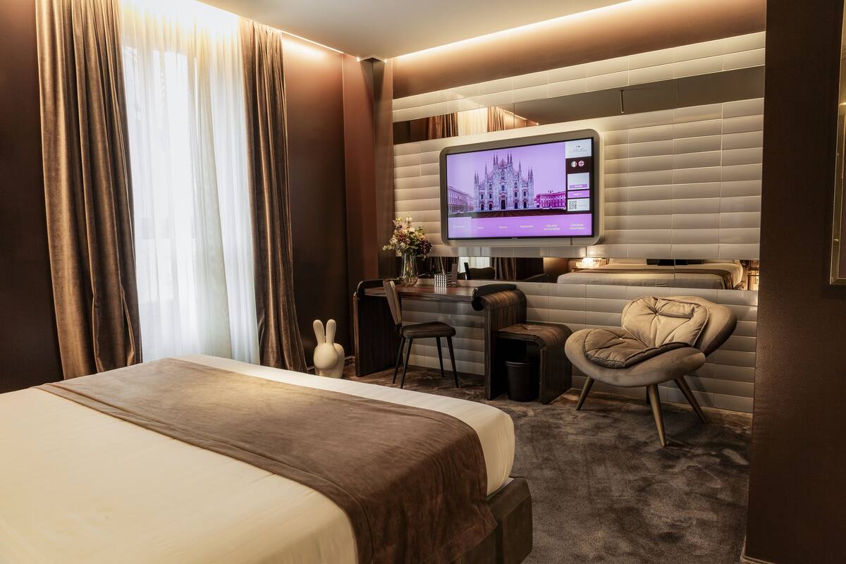 Une chambre d’hôtel avec un grand lit, un bureau avec un ordinateur, une chaise et un téléviseur fixé au mur.