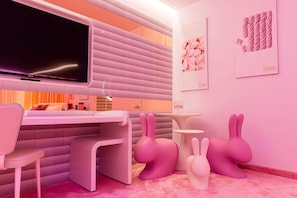 Une chambre d’hôtel moderne équipée d’un téléviseur à écran plat, d’un canapé rose, d’un bureau et de deux fauteuils en forme de lapin.