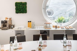A modern dining area with a round window, a coffee machine, and a variety of food and drink options. - Innside Milano Torre Galfa (Milan)