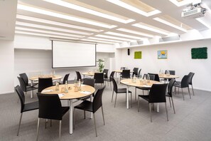 A modern conference room with round tables, black chairs, a projector screen, and a whiteboard. - Innside Milano Torre Galfa (Milan)