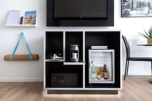A modern living space with a flat-screen TV, a coffee maker, a mini-fridge with beverages, a yoga mat, and a remote control on a shelf. - Innside Milano Torre Galfa (Milan)