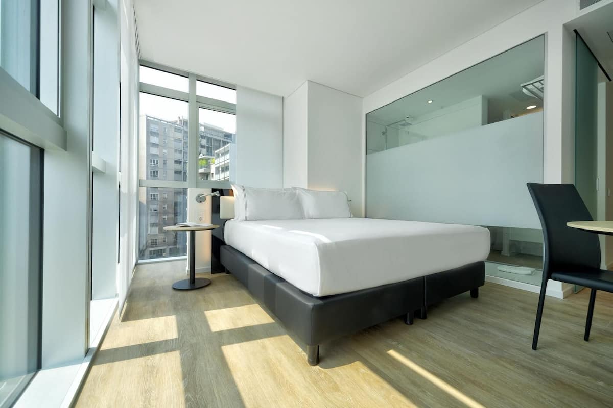 A modern hotel room with a large bed, a desk, and a chair.