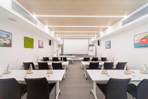 Ett konferensrum med vita bord, svarta stolar och en projektorduk.