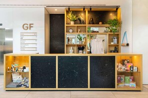 Un mostrador de recepción de hotel con encimera de mármol, una vitrina de madera con objetos y un cartel que enumera los tipos de habitaciones.