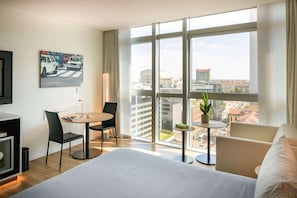 A hotel room with a large bed, a dining table, two chairs, a small table with a plant, and a painting of cars on the wall. - Innside Milano Torre Galfa (Milan)